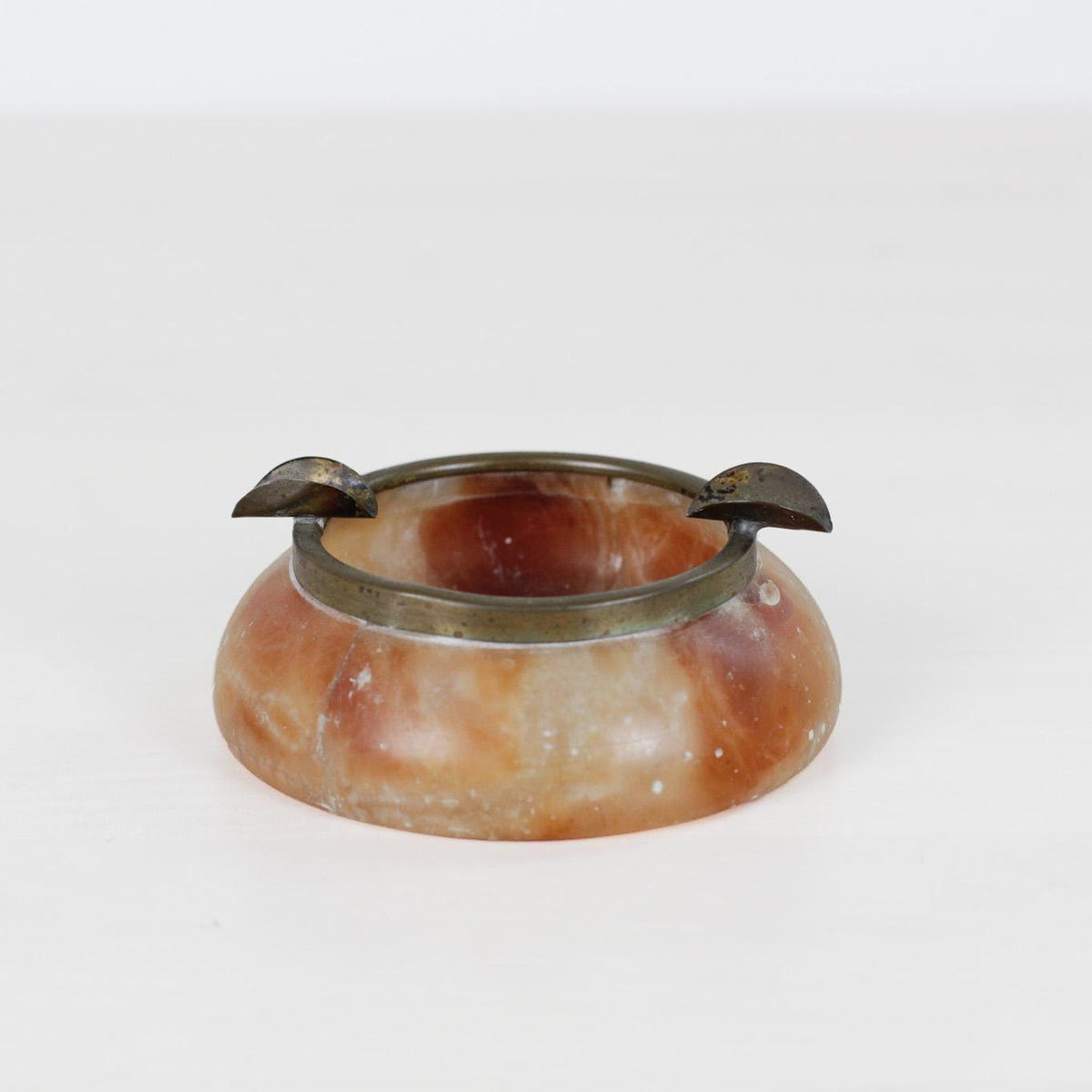 A small round stone or ceramic vessel with a warm brown and cream marbled finish, featuring a dark metallic rim and two small side handles, photographed on a plain white background.