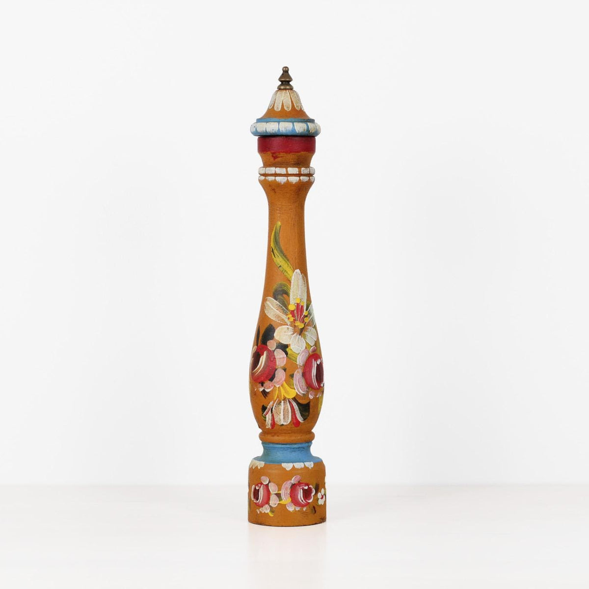 A tall, slender decorative object with a pointed top and a colorful floral hand-painted design, standing upright on a white surface against a white background.