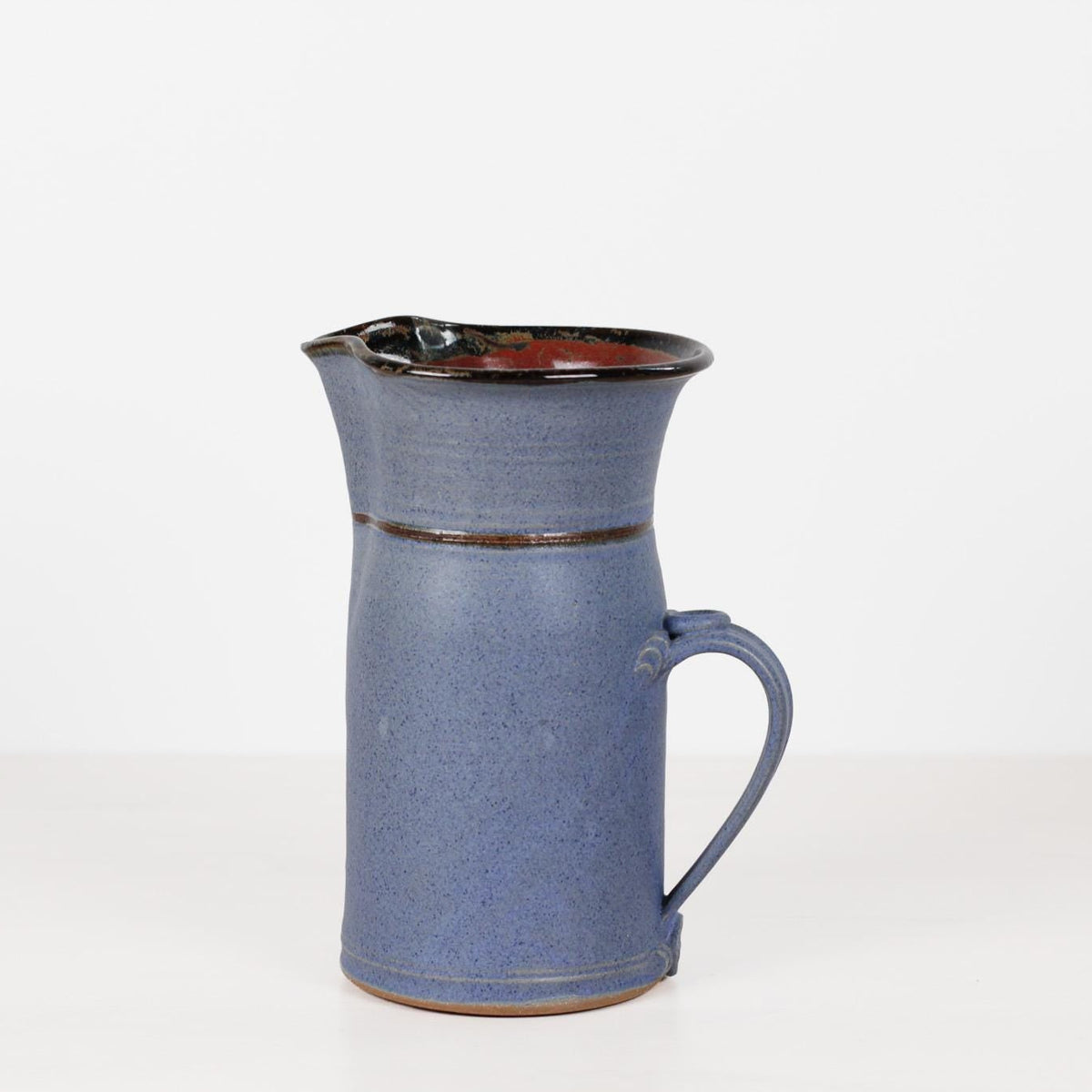 A handmade ceramic pitcher with a speckled slate blue body, a dark brown glazed interior, and a matching handle, set against a plain white background.