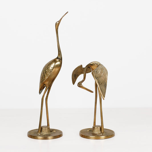 Two metallic heron figurines on round bases, photographed against a clean white studio background.