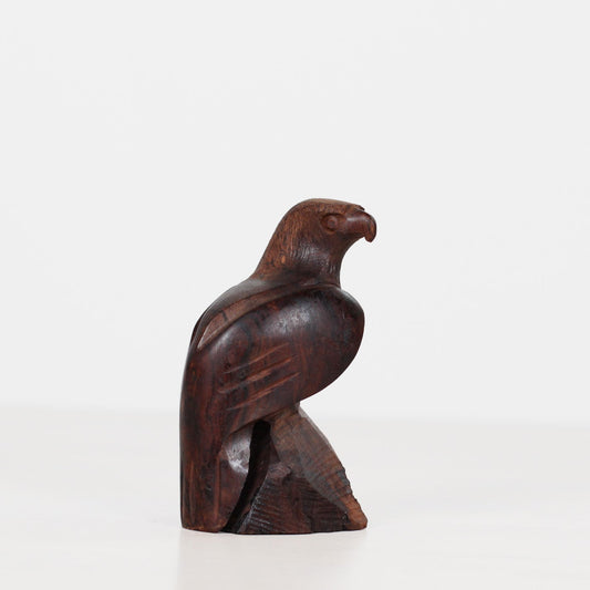 A small carved wooden bird figurine, shaped like a falcon or hawk in profile, shown on a plain white studio background.