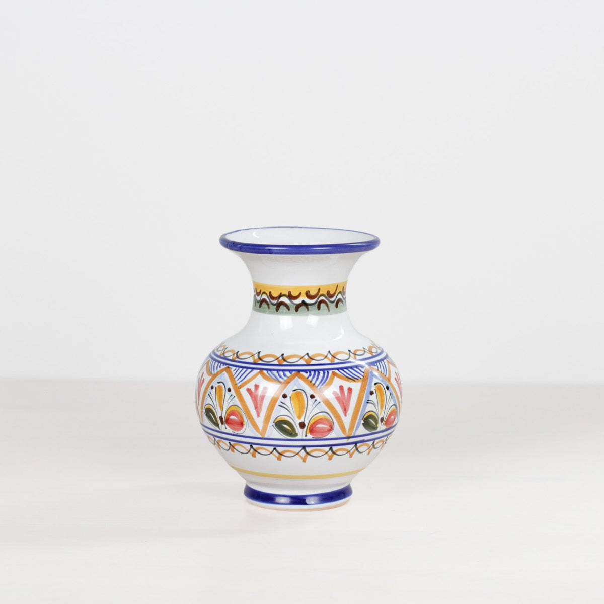 A small white ceramic vase with a narrow neck and flared rim, decorated with colorful geometric and floral patterns in blue, orange, yellow, green, and red, set against a plain white background.