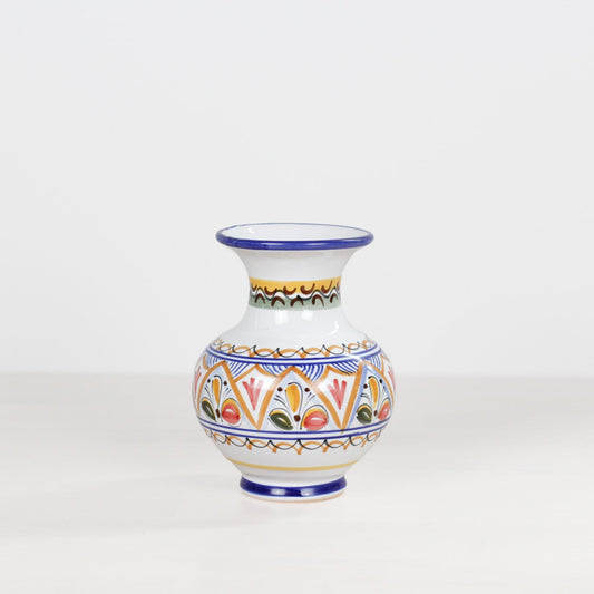 A small white ceramic vase with a narrow neck and flared rim, decorated with colorful geometric and floral patterns in blue, orange, yellow, green, and red, set against a plain white background.
