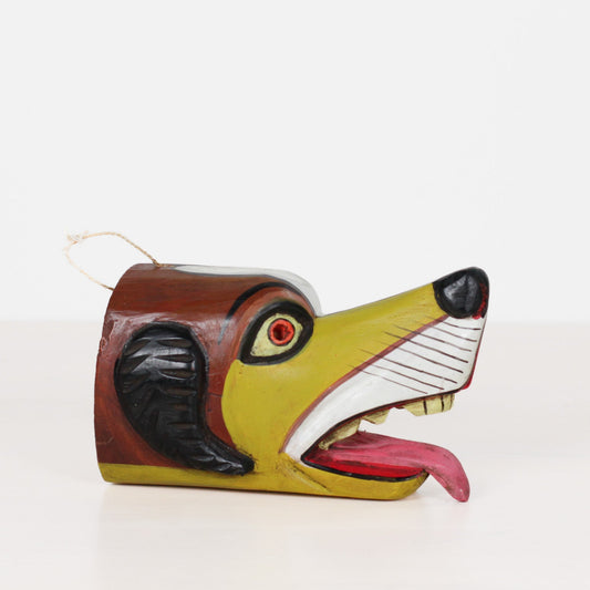 A hand-painted wooden dog head hanging ornament with a white string loop, featuring a yellow-green face, brown head, black ears, and an open mouth showing a pink tongue and white teeth.
