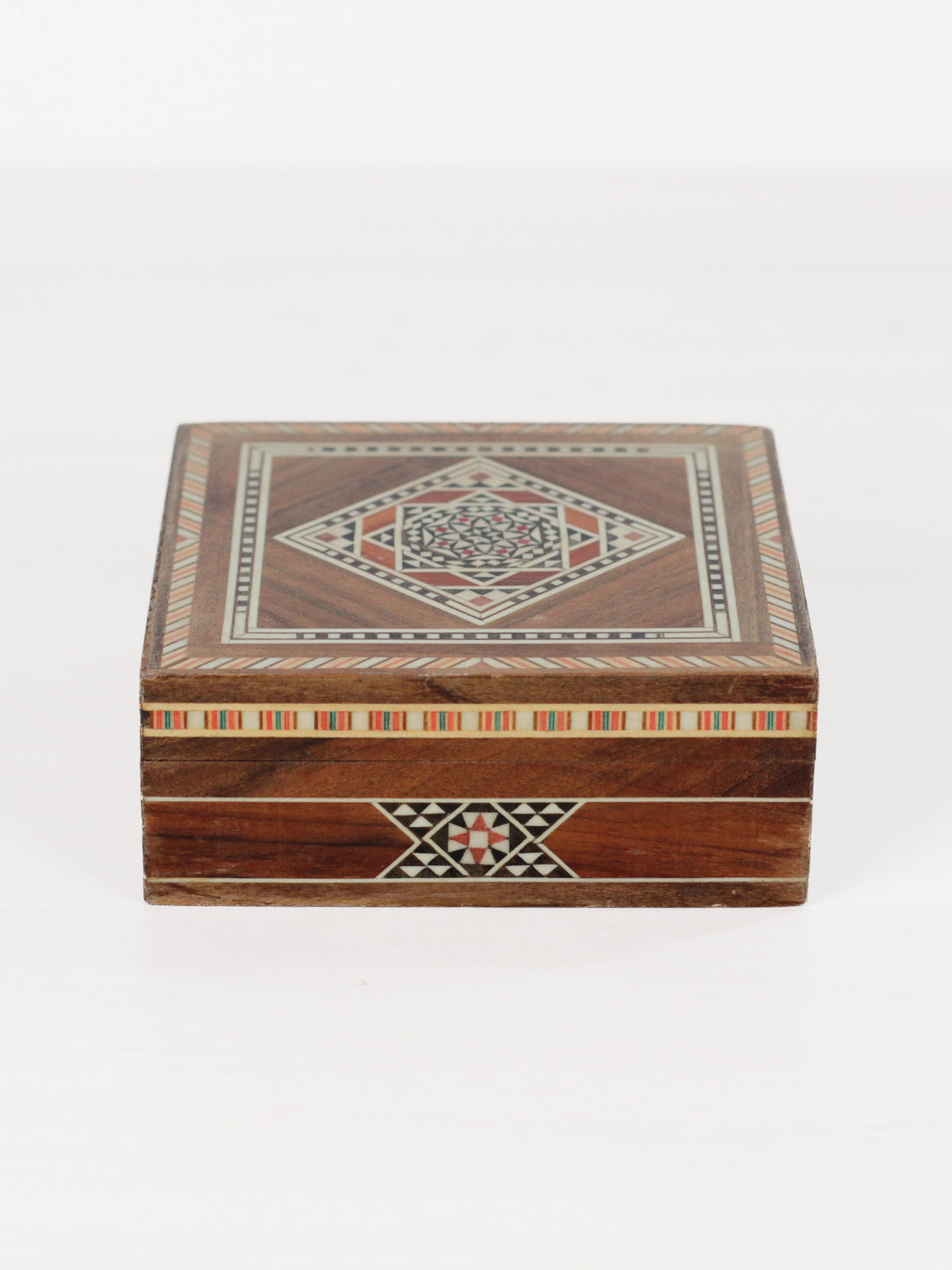 A square wooden keepsake box with intricate geometric inlay patterns on the lid and front, set against a plain white background.