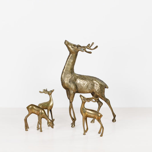 Three metallic deer figurines in a warm gold/brass finish, including one large stag and two smaller fawns, displayed on a clean white surface against a white background.